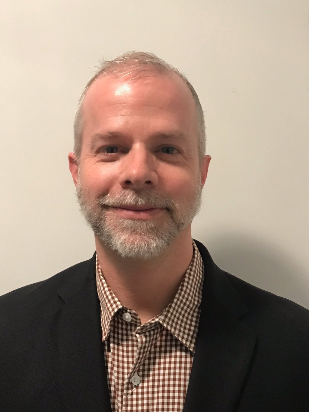 Alexander Slagg with grey beard, black sport coat, checkered button down shirt