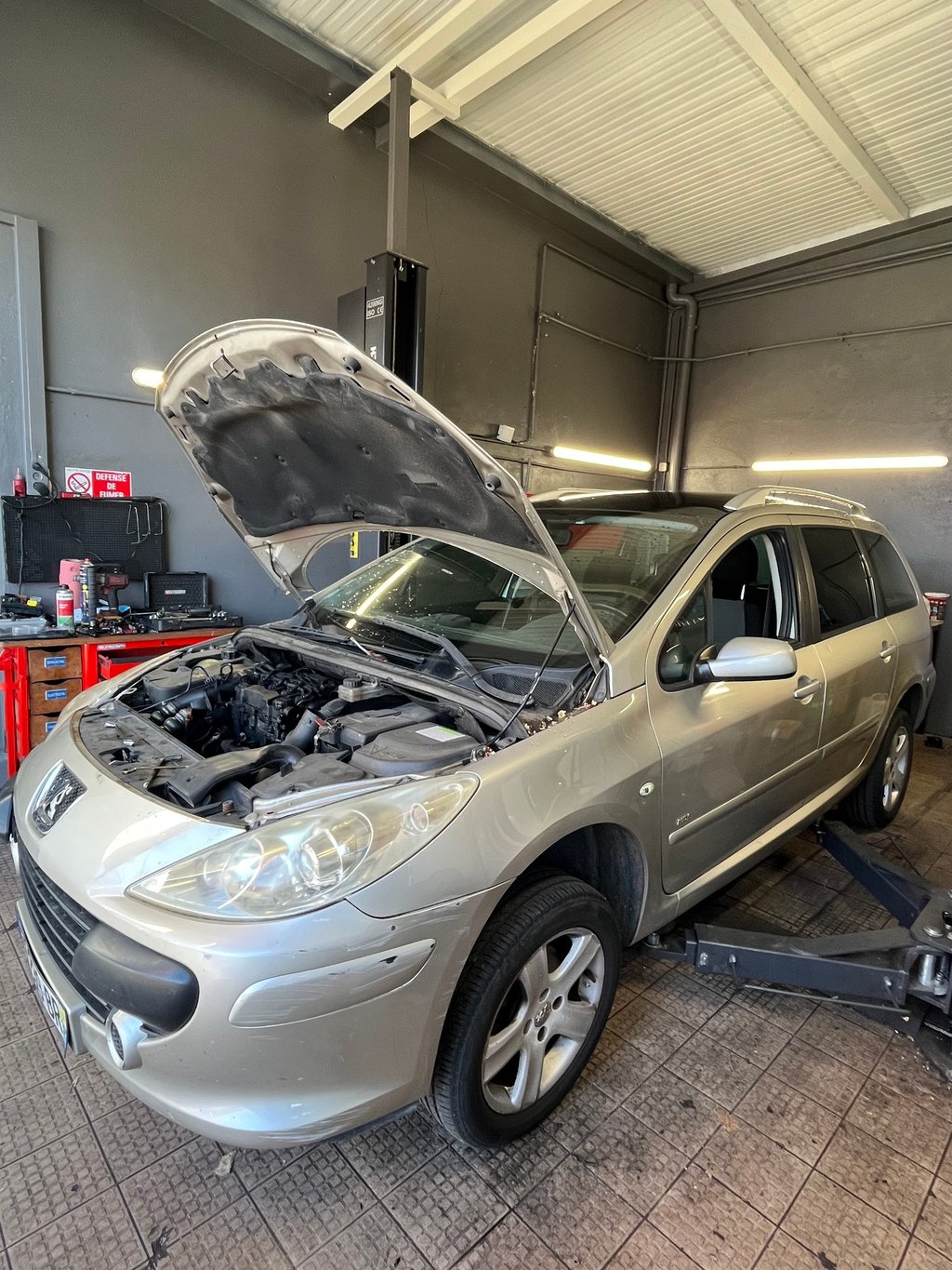 a car with a in a garage with mechanics working on it