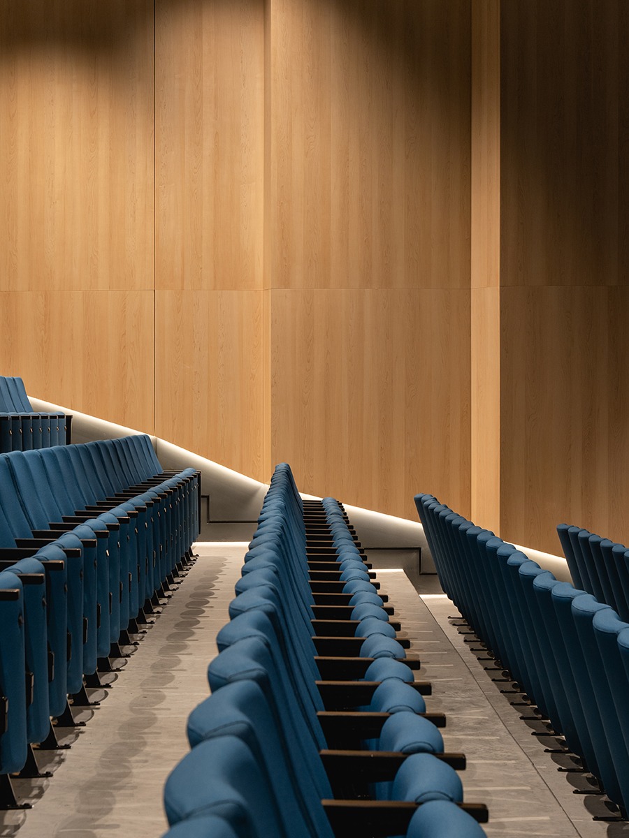 a wood clad auditorium with rows of blue chairs
