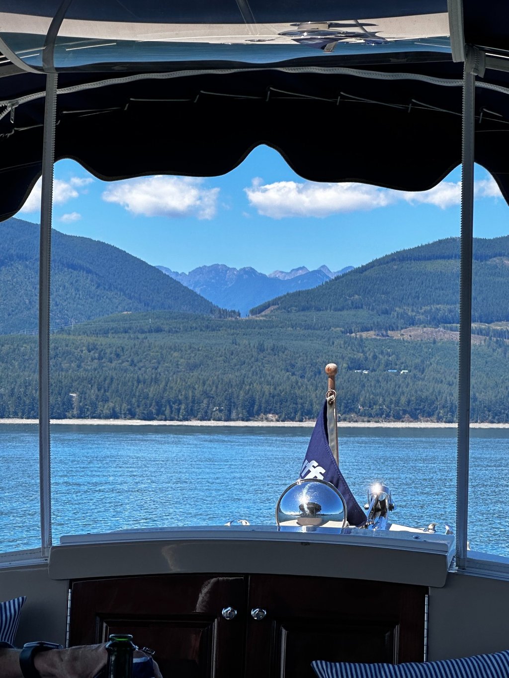 front of boat with flag on pristine water facing majestic mountains