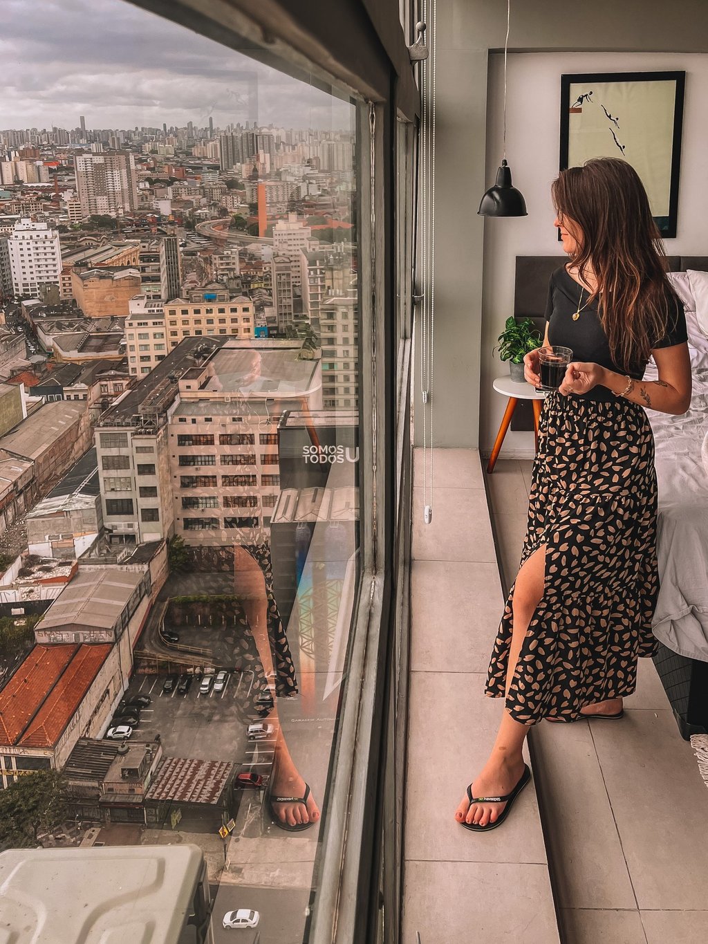 Uma pessoa em pé com uma xícara de café nas mãos, enquanto avista a cidade de São Paulo do topo.