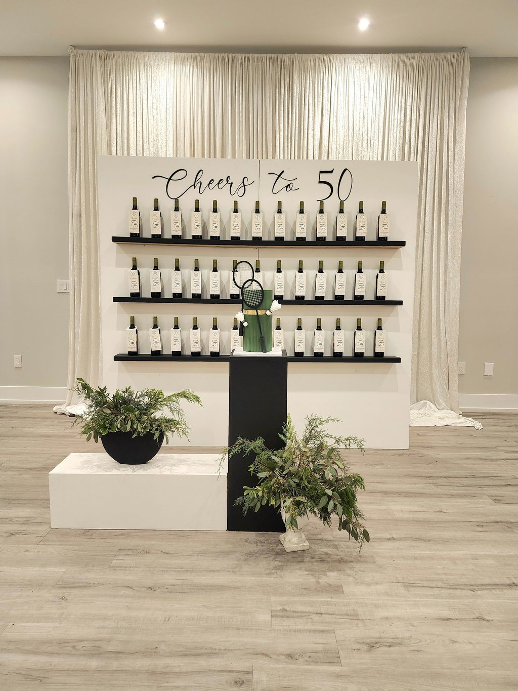 a backdrop display of wine bottles as a favor wall for a 50th birthday celebration