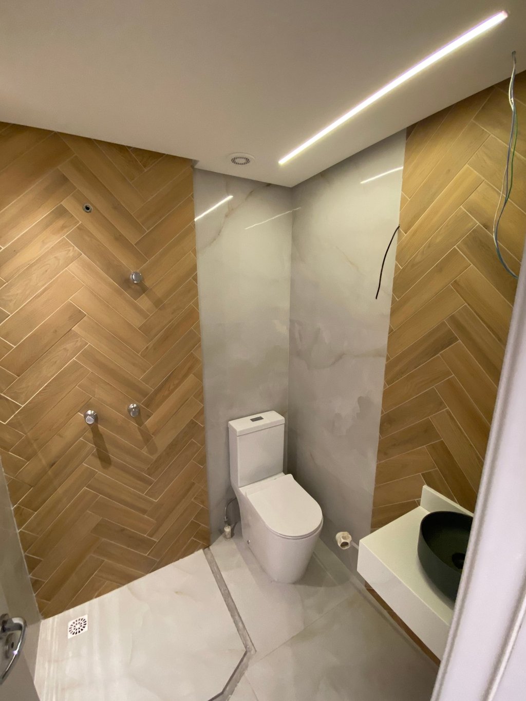 Banheiro reformado pela Nattú Engenharia com porcelanato claro e madeira em estilo espinha de peixe