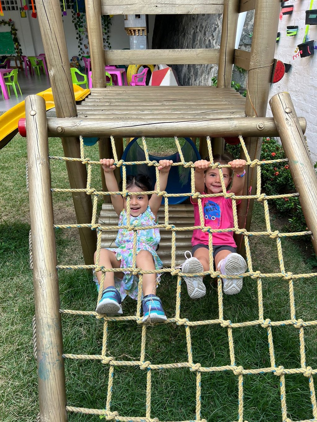 Niñas colgadas de malla en playground de madera en un pasto en Ukelele Jardín Infantil