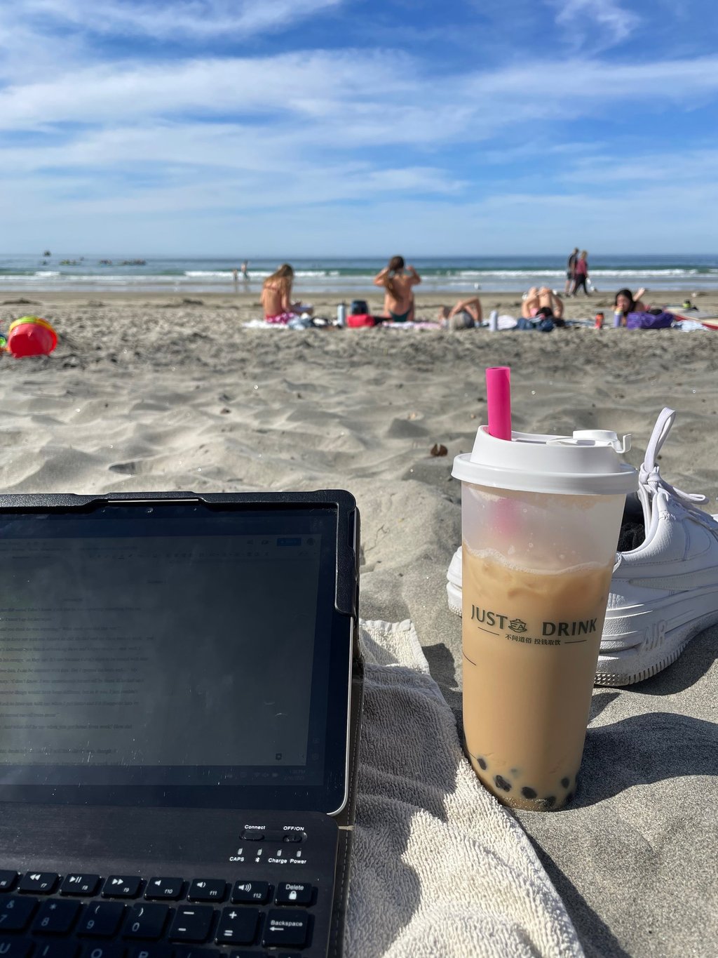 a laptop computer and a cup of brown sugar milk tea with boba sitting on a beach