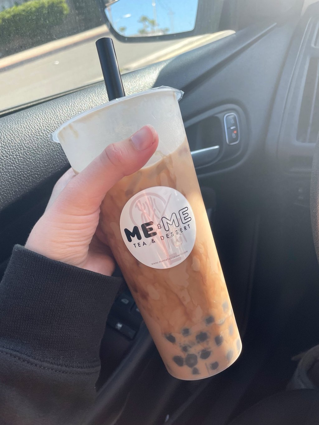 a person holding a cup of brown sugar milk tea with boba in a car