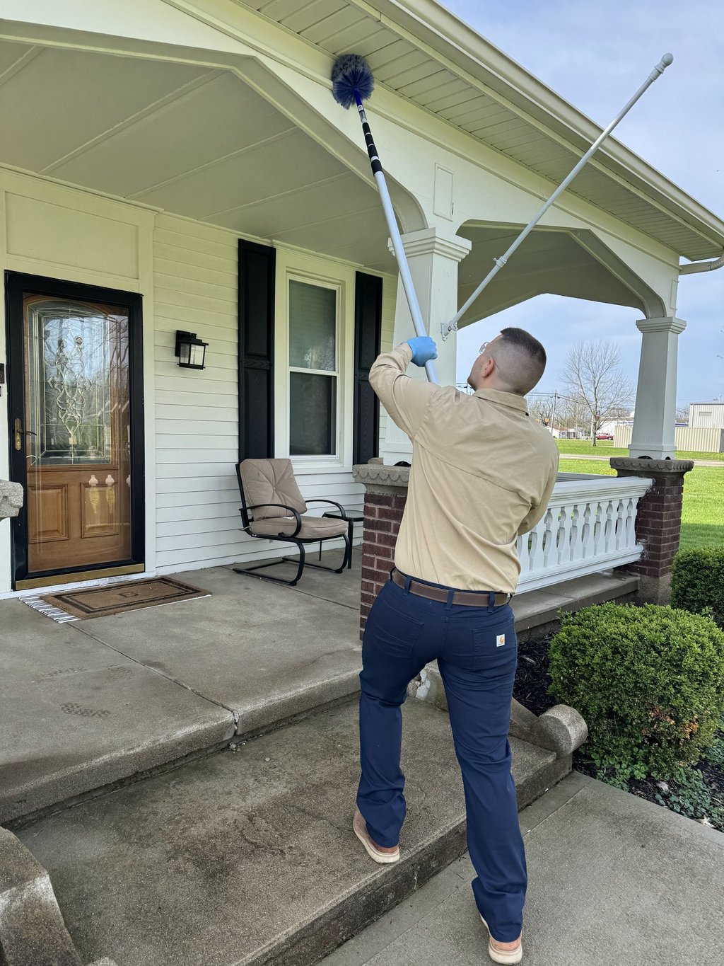 Pest control technician removing spider webs from house