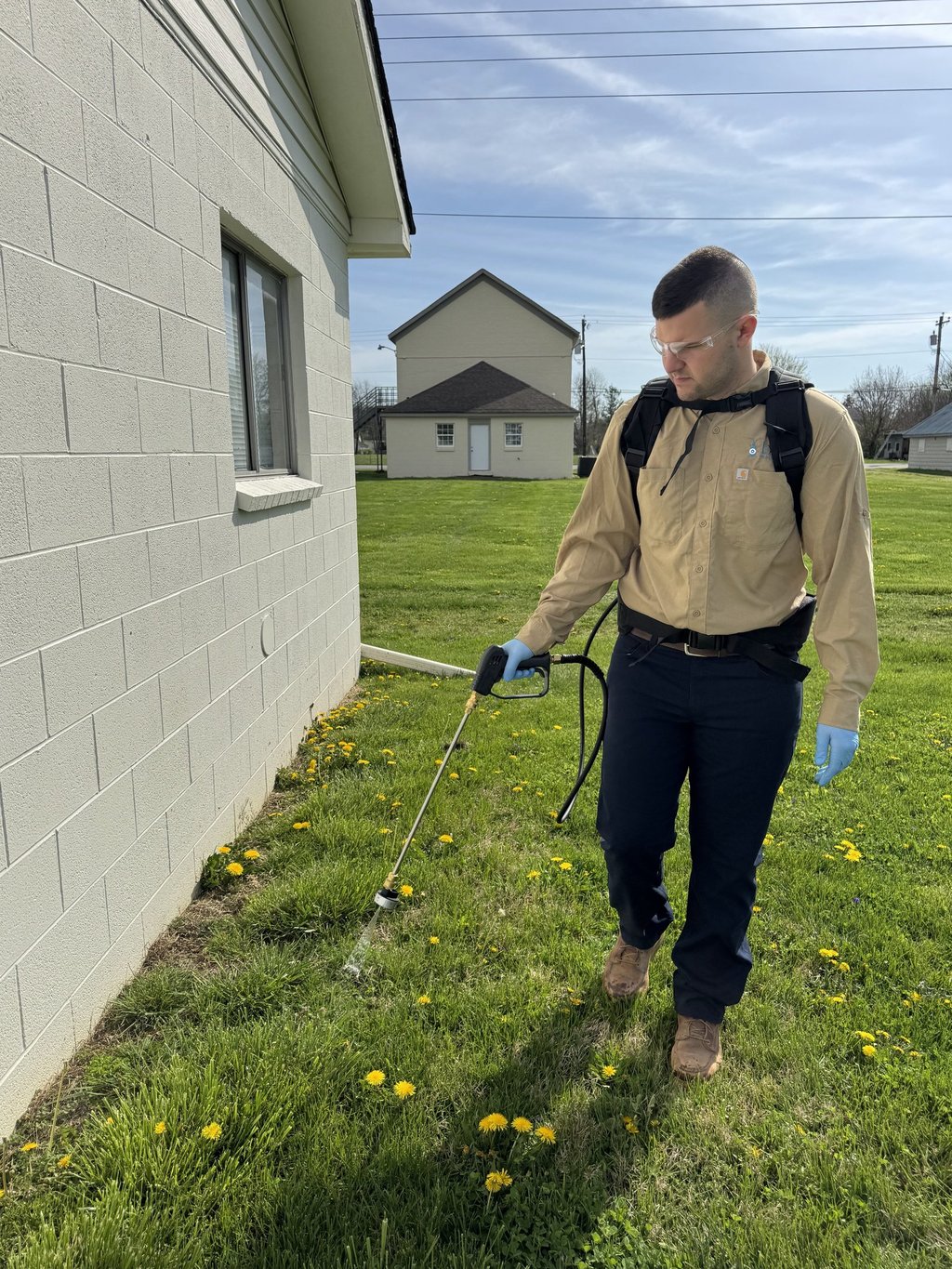 Pest control technician spraying around foundation of garage