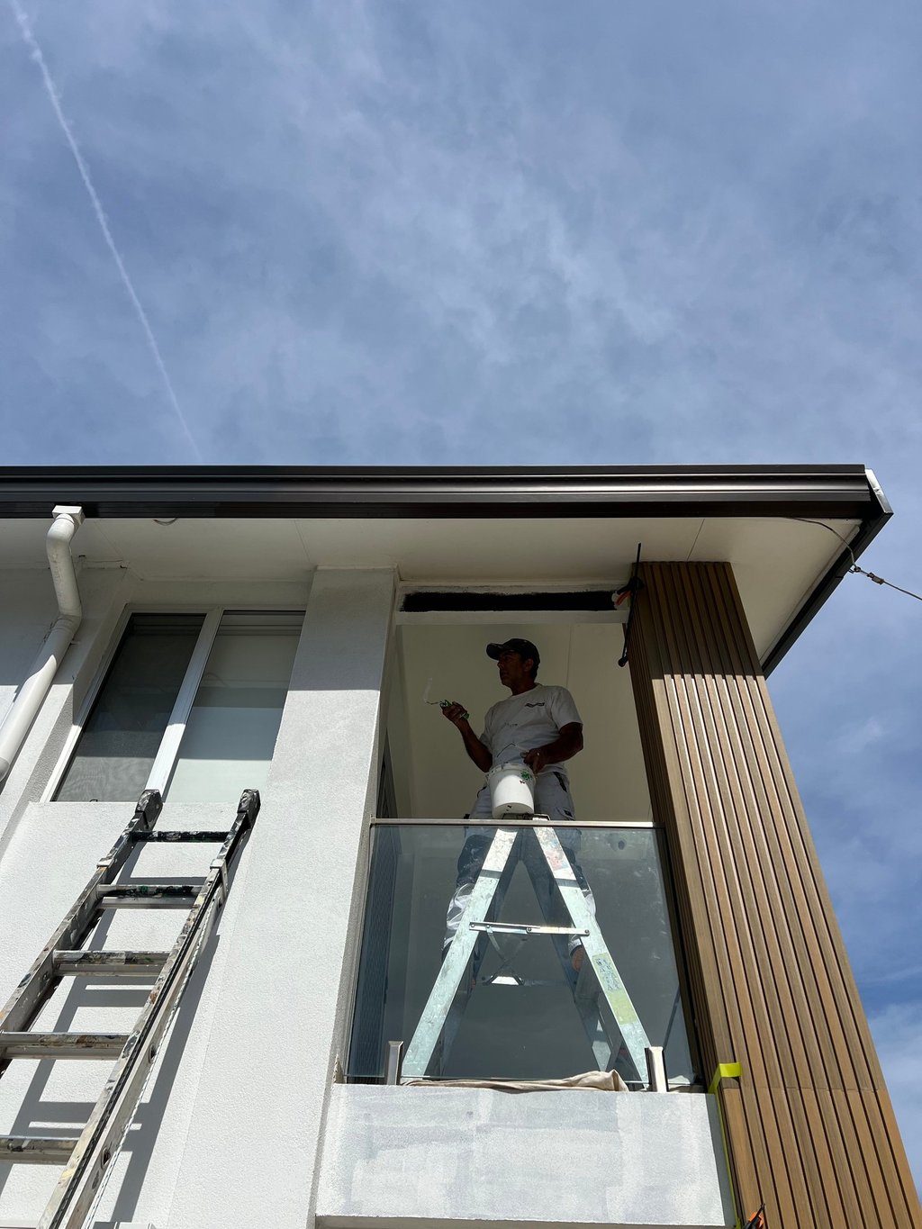 Painter in oster bay on  ladder to reach up to a window
