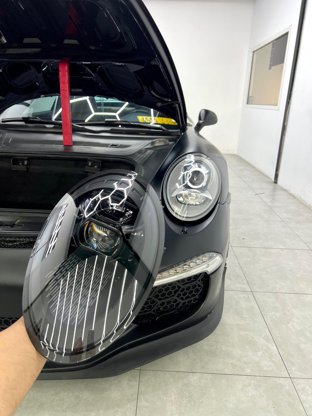 Close-up of a custom black LED headlight being installed on a matte black Porsche 911 GT3.