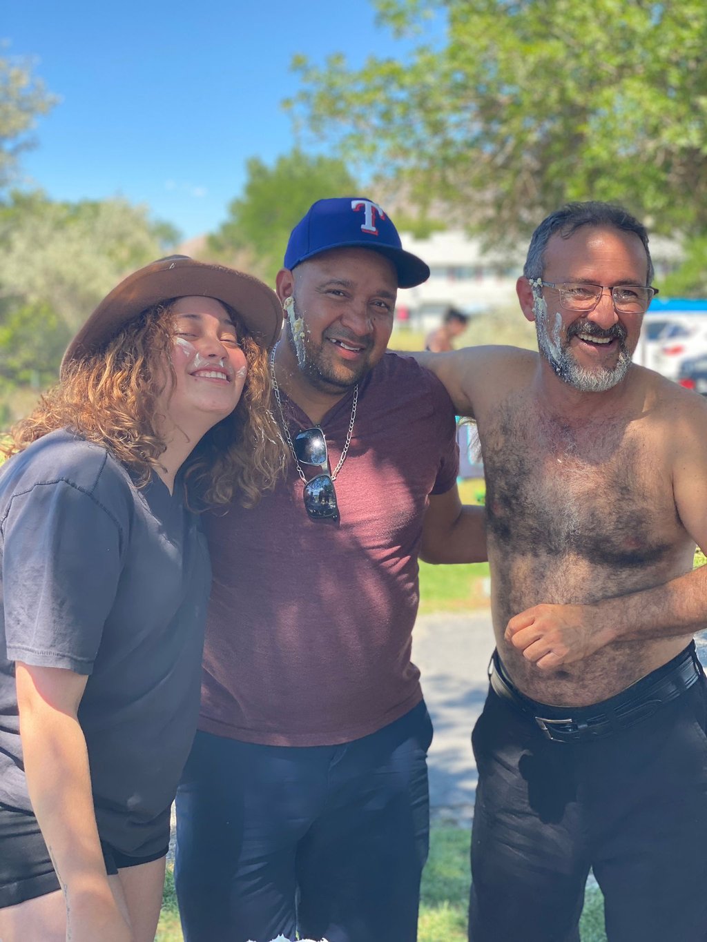 A group of happy friends smiling outdoors with cake frosting on their faces during a summer celebration.