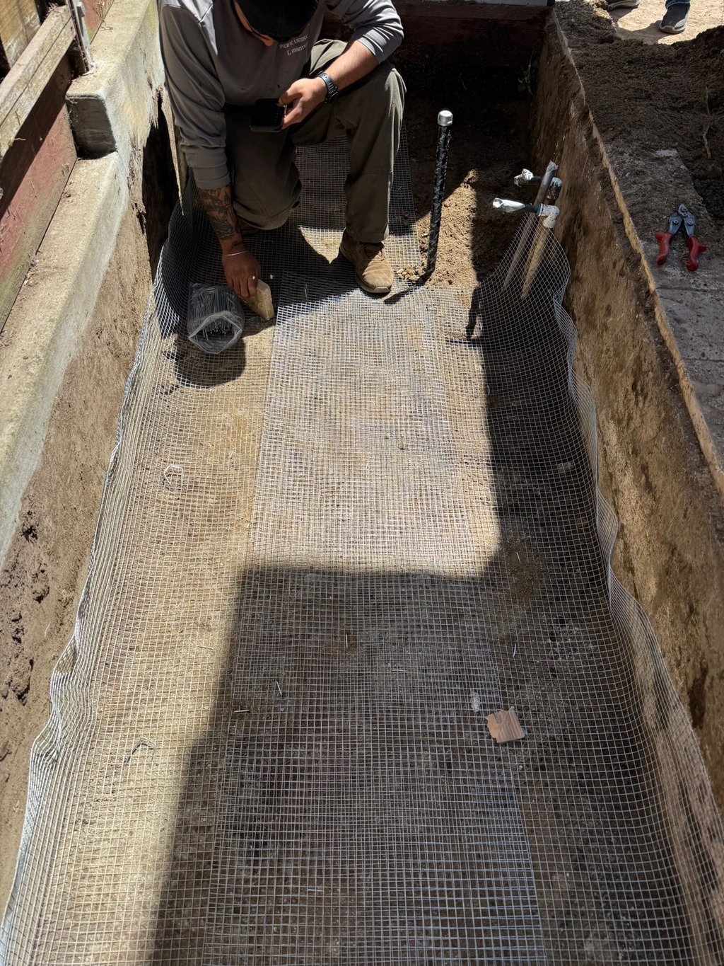 A contractor installs wire mesh hardware cloth in a trench for gopher and rodent proofing a foundation.