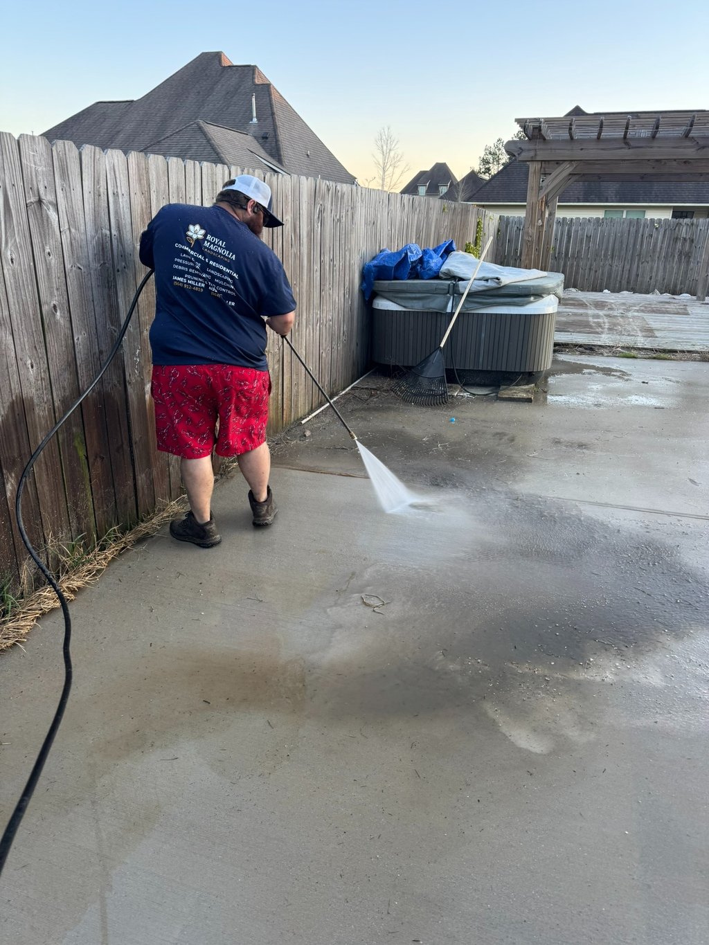 Professional pressure washing service cleaning a dirty concrete patio and wood fence in a residential backyard.