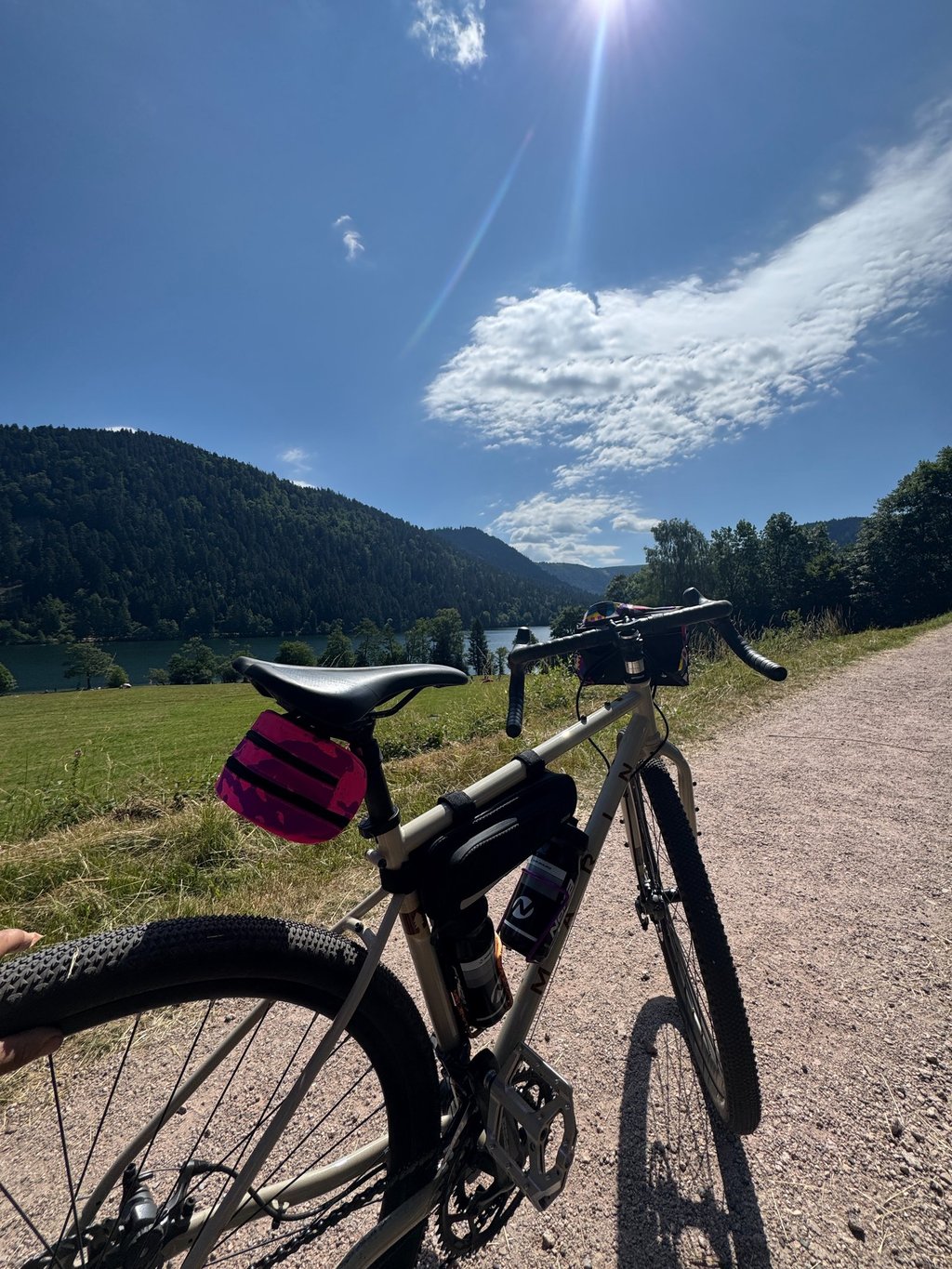 Gravel bike with bikepacking bags parked on a scenic dirt trail overlooking a lake and mountains.