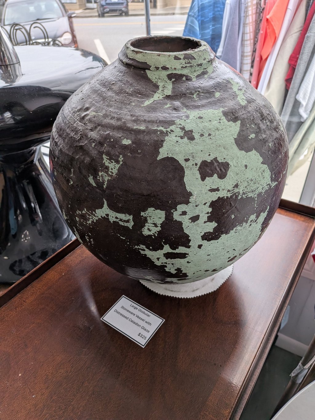 Large globular stoneware vessel with a distressed celadon glaze on a wooden table.