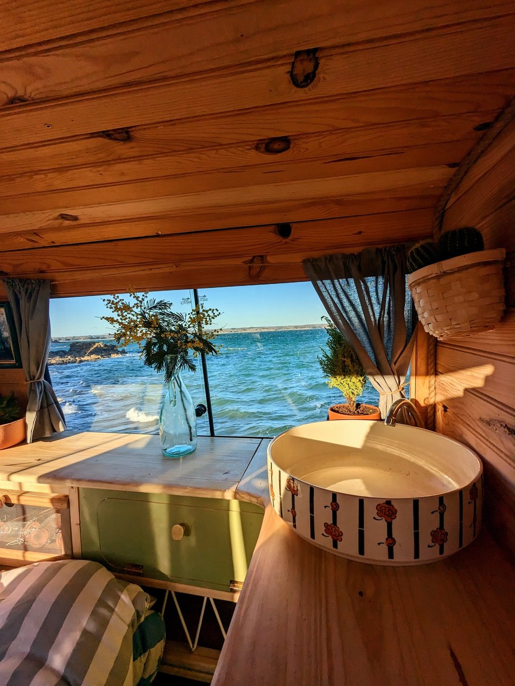 Aménagement van vintage avec vue sur l'océan en Bretagne, intérieur bois et décoration artisanale.