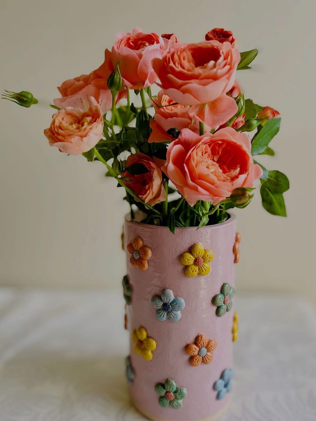 A handmade vase with colourful flower decoration filled with roses
