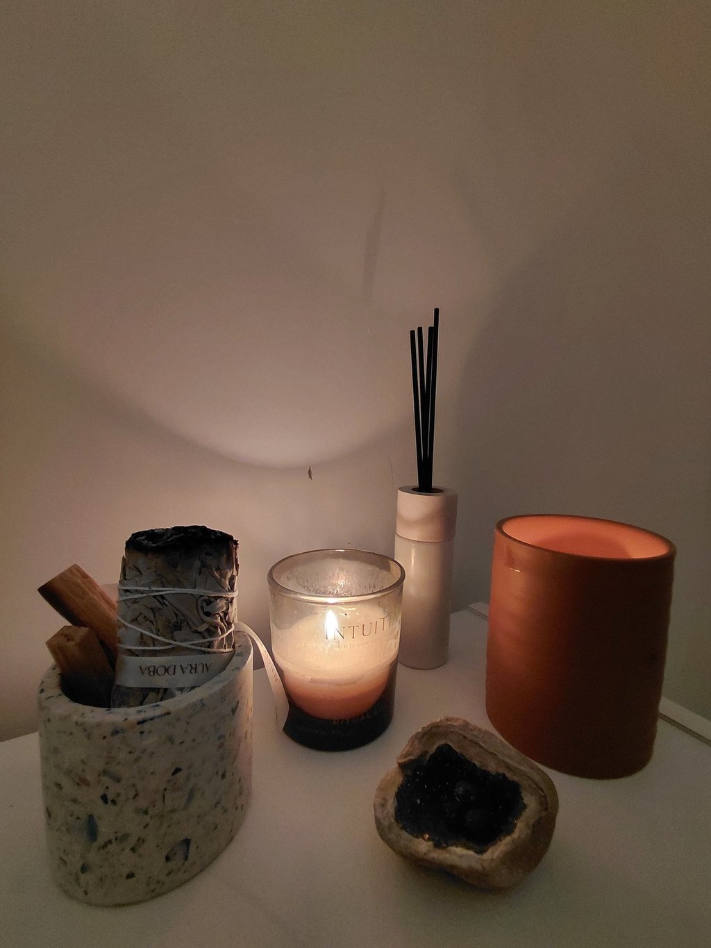 A spiritual wellness set featuring a lit scented candle, white sage smudge stick, and palo santo.