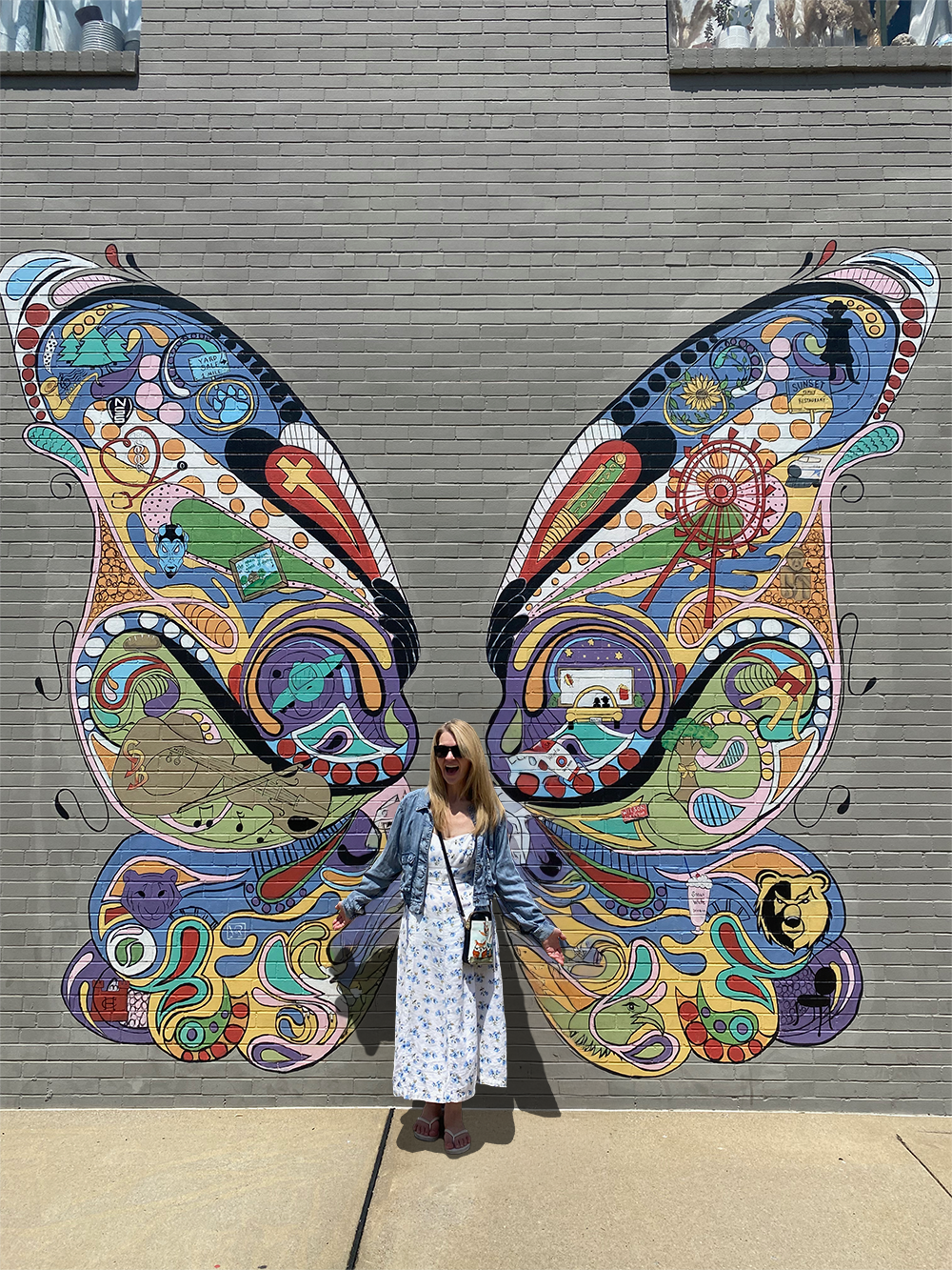 Nini standing against a wall with a mural of butterfly wings