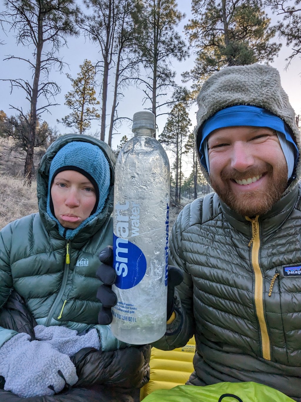 Moose and Bugs making silly faces in a selfie while Moose holds a frozen water bottle at a camp.