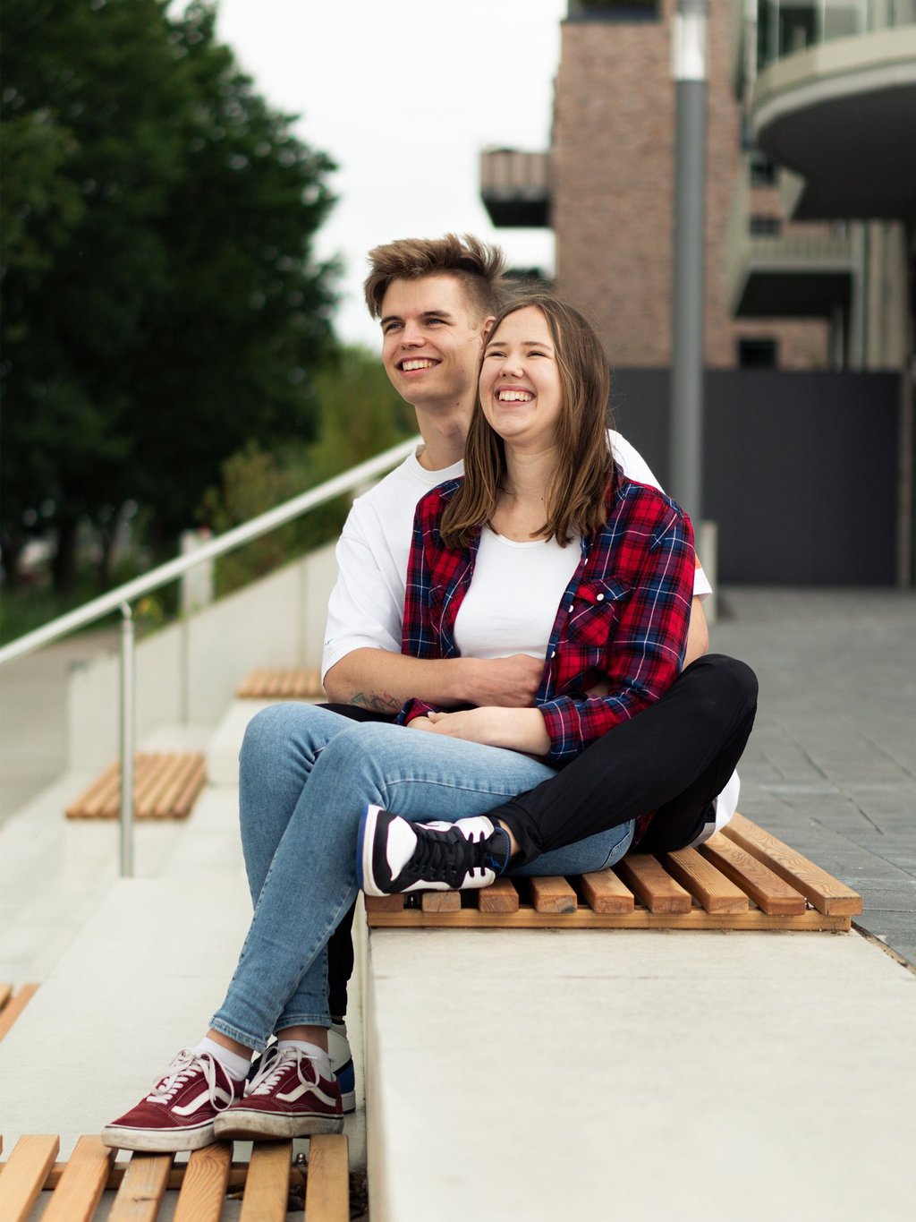 Lachendes Paar sitzt entspannt auf einer Bank bei einem urbanen Paarshooting. Foto von Joel Pingel.