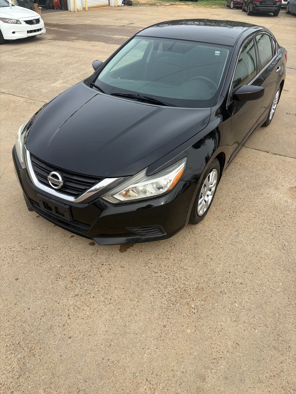Black Nissan Altima sedan parked on a concrete lot at a used car dealership.