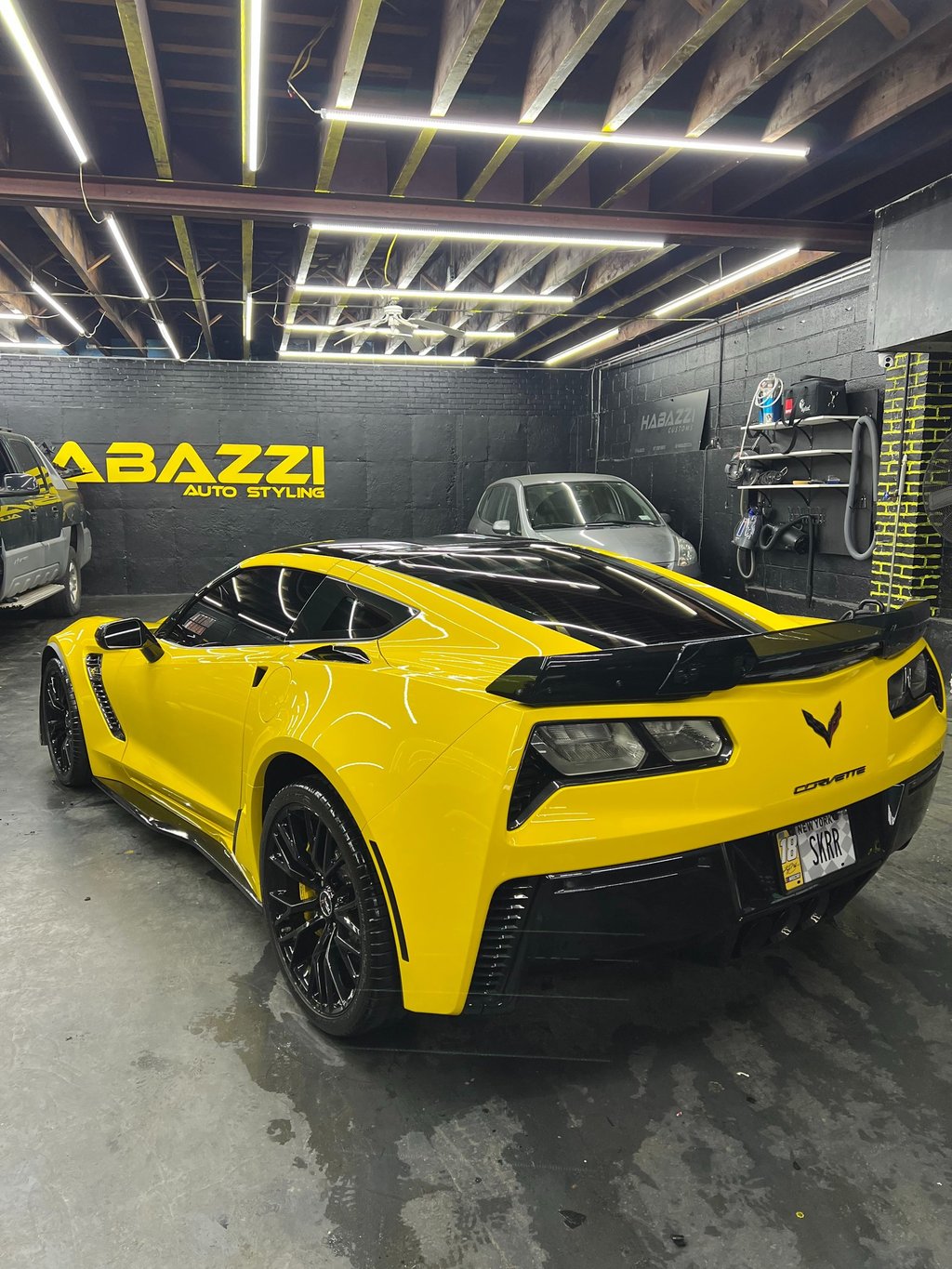 Yellow Chevrolet Corvette C7 with black trim inside a professional auto styling and car detailing garage.