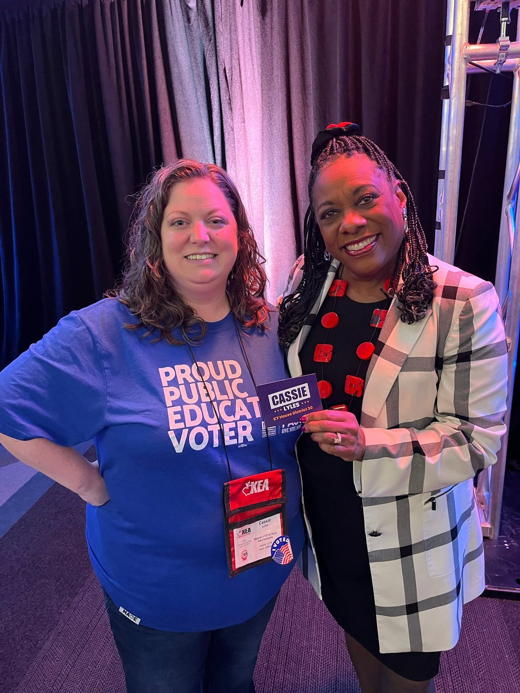 Woman in blue shirt standing with a black woman holding a campaign sticker