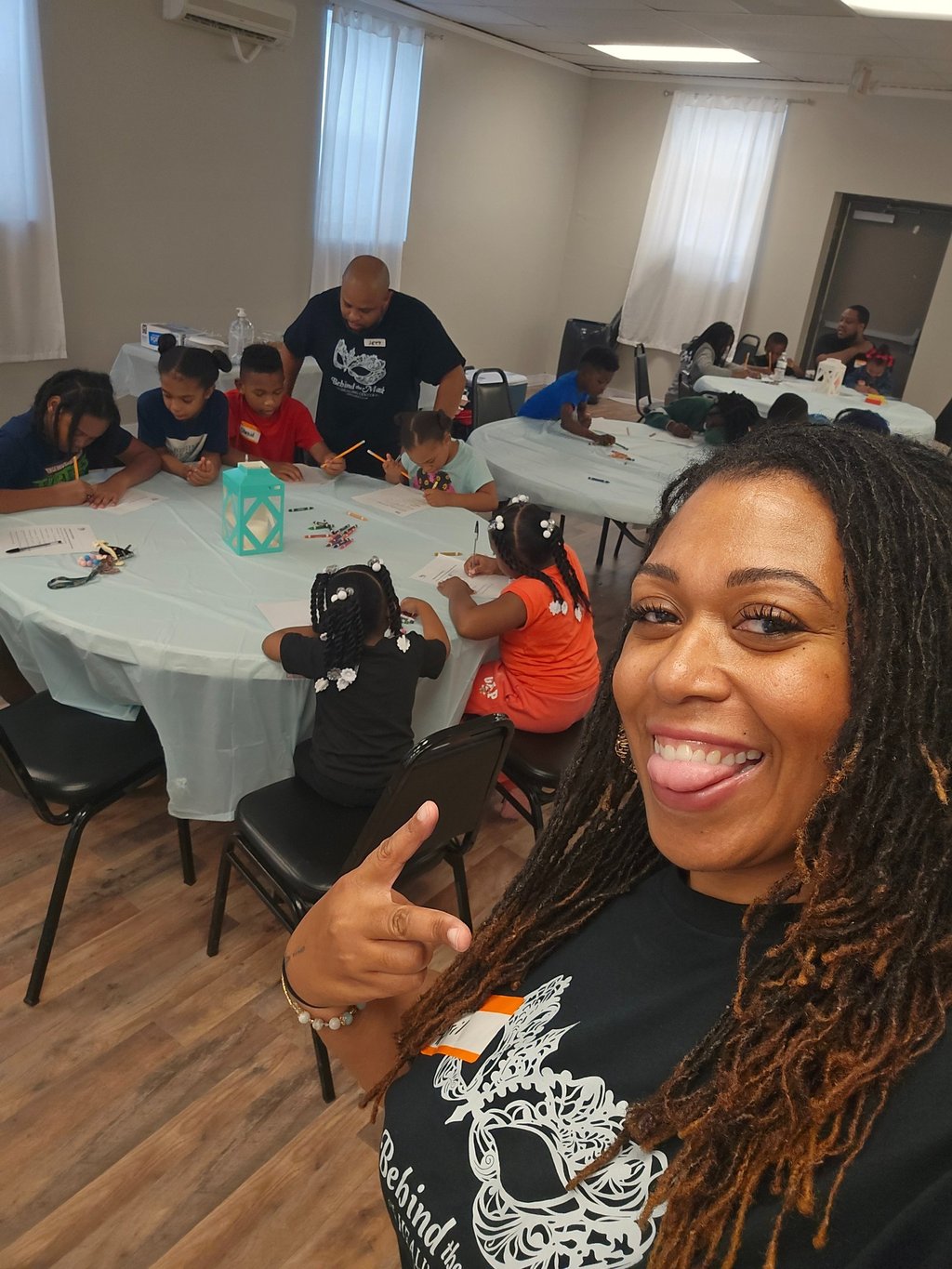Smiling teacher takes a selfie while students engage in a creative art activity at a youth community center.