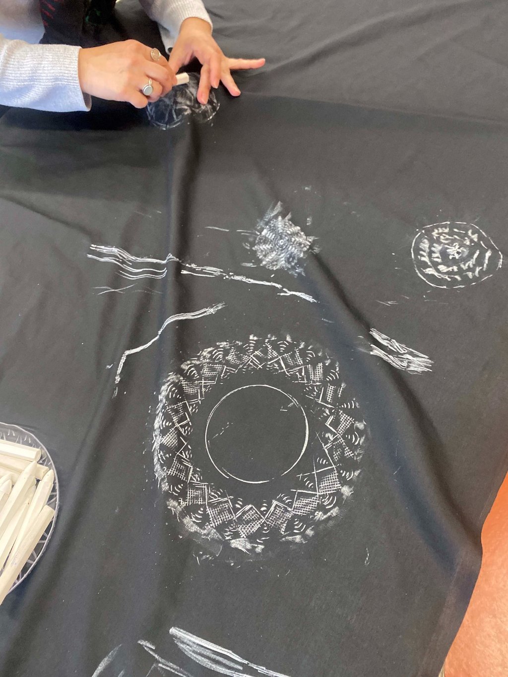 A young person using a stick of chalk on fabric to rub the outlines of a shape underneath the fabric.