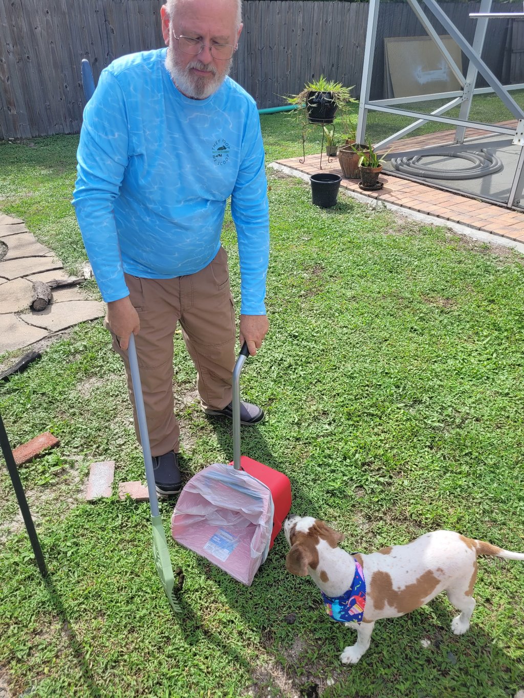 Robert using a sanitized scooper to remove waste from a customers back yard, small dog watching him