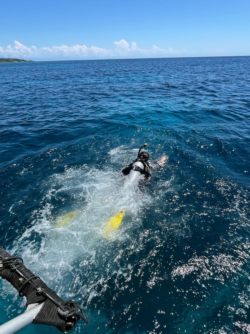 A scuba diver with yellow fins jumps into the deep blue ocean water from a boat during a diving excursion.