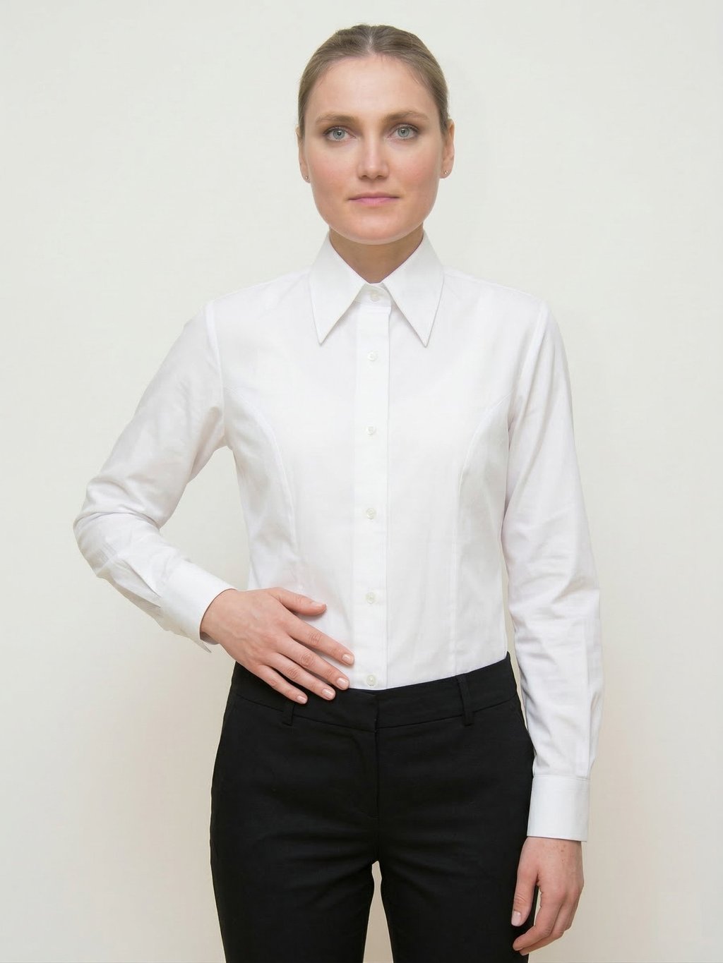 Mujer profesional con una clásica camisa blanca de manga larga abotonada y pantalones negros.