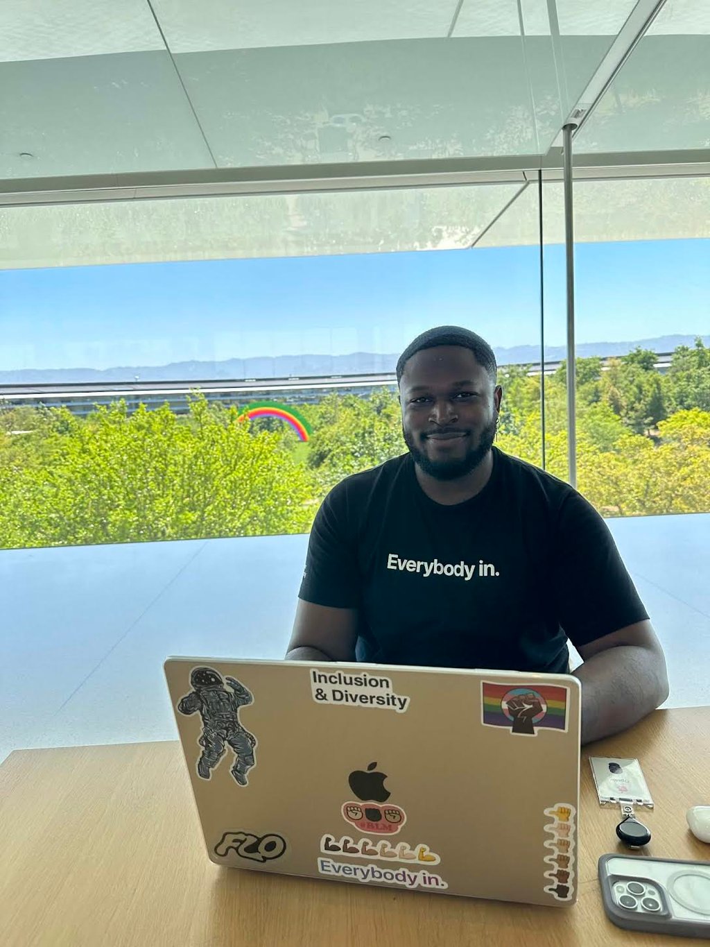 A young professional smiles and wears a black shirt that says, "Everybody in."
