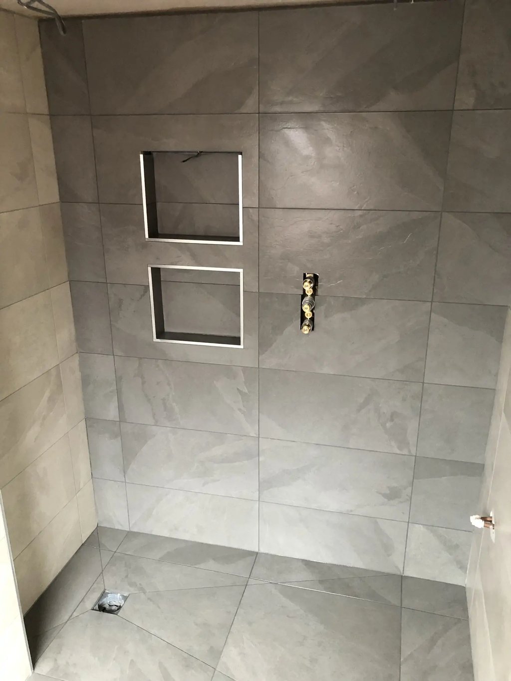 Modern tiled shower wall with recessed storage niches during bathroom renovation in Brighton.