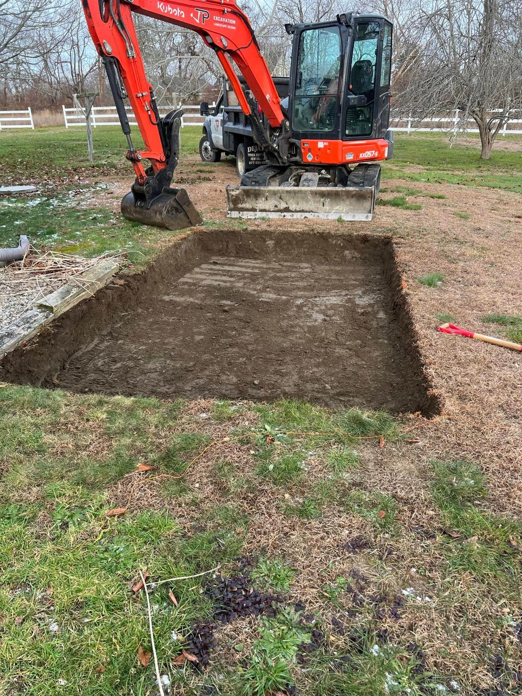 Orange Kubota mini excavator completing a precise rectangular ground excavation for a backyard project.