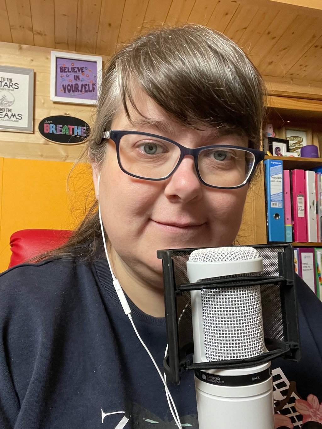 Laura Dumbleton at her recording setup with a microphone and BREATHE sign on the wall behind her