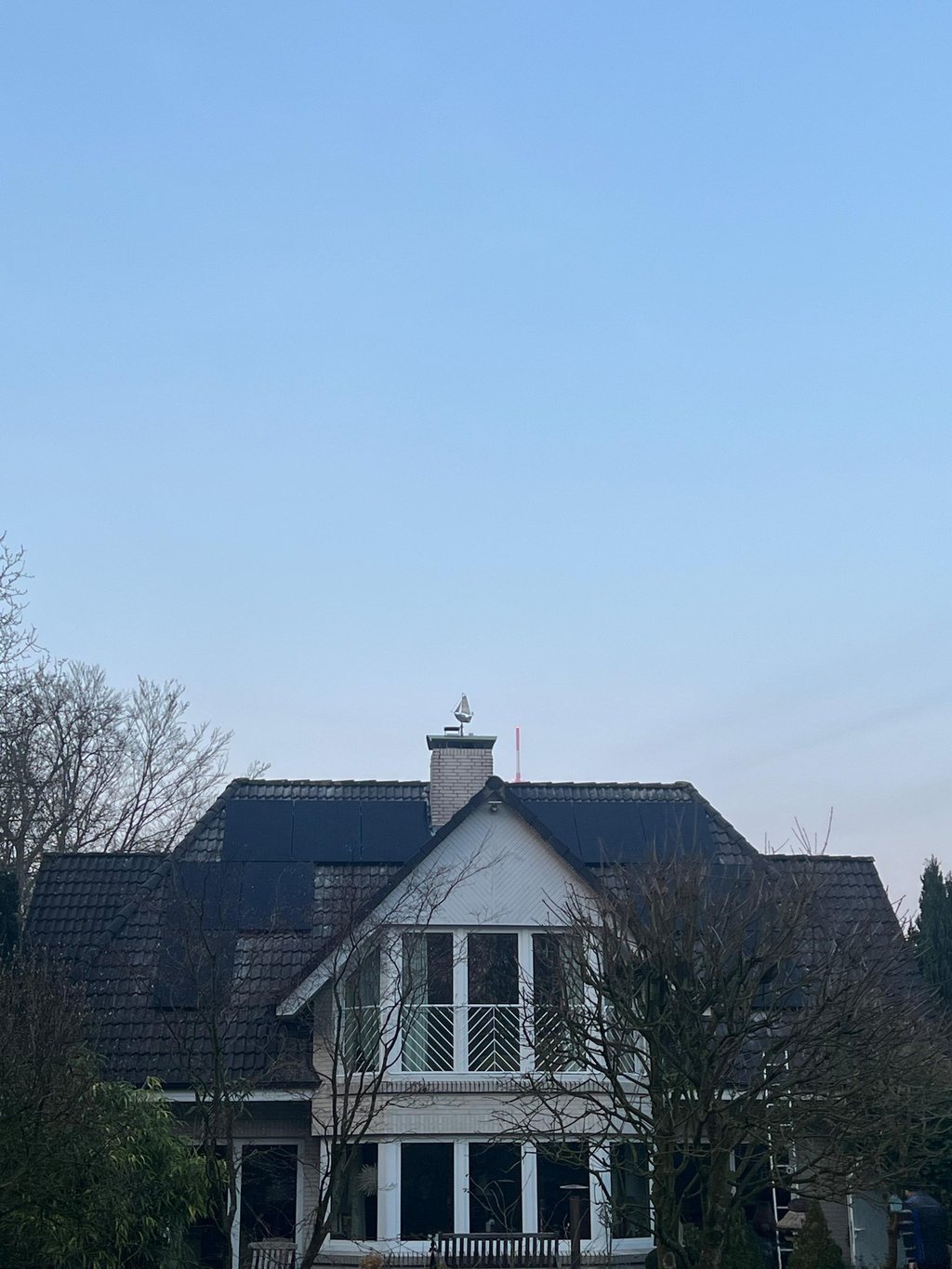 Modern white house featuring a dark tiled roof with rooftop solar panels installed under a clear blue sky.