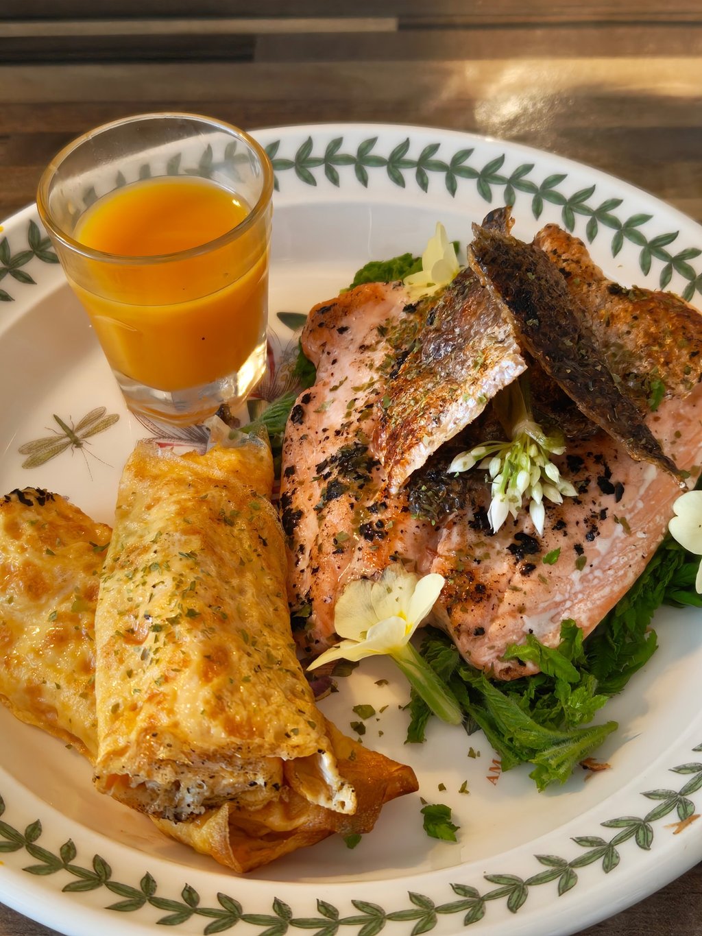 Rolled egg, salmon with crispy skin, wild garlic flower garnish, sea buckthorn juice