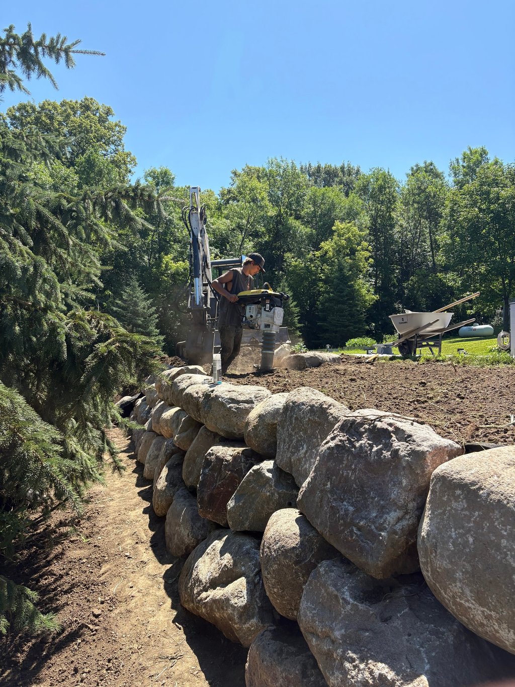 Arcadia Landscapes employee compacting dirt around boulder wall