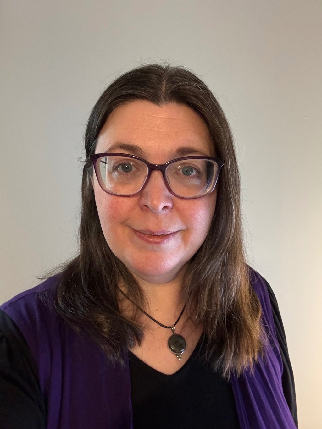 A woman with brown hair wearing glasses and smiling.