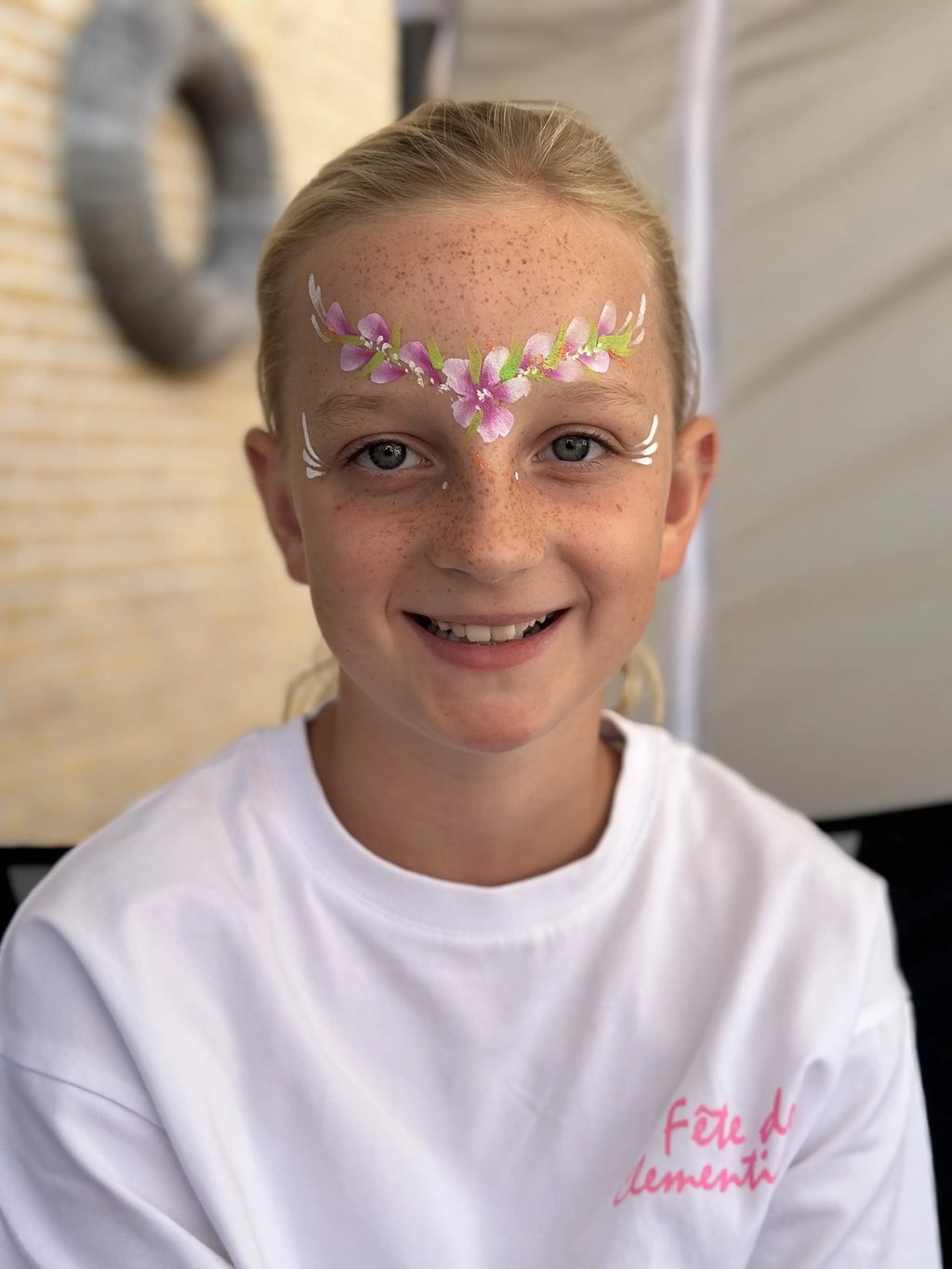 Glimmachend meisje met een elegant geschminkte bloemenkrans in roze en groen op haar voorhoofd.
