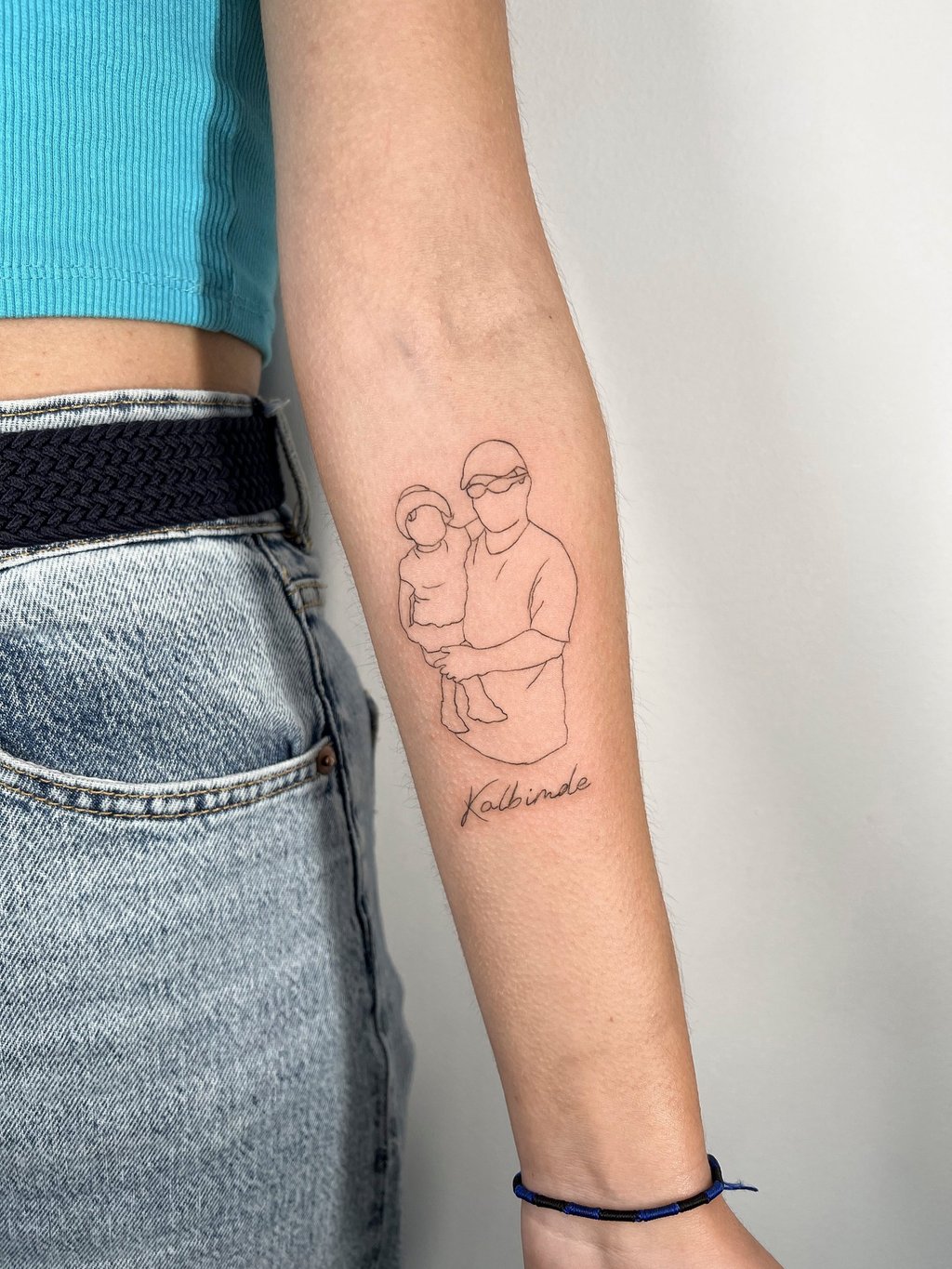 Tatouage d'un enfant dans les bras d'un adulte en fine line sur l'avant-bras