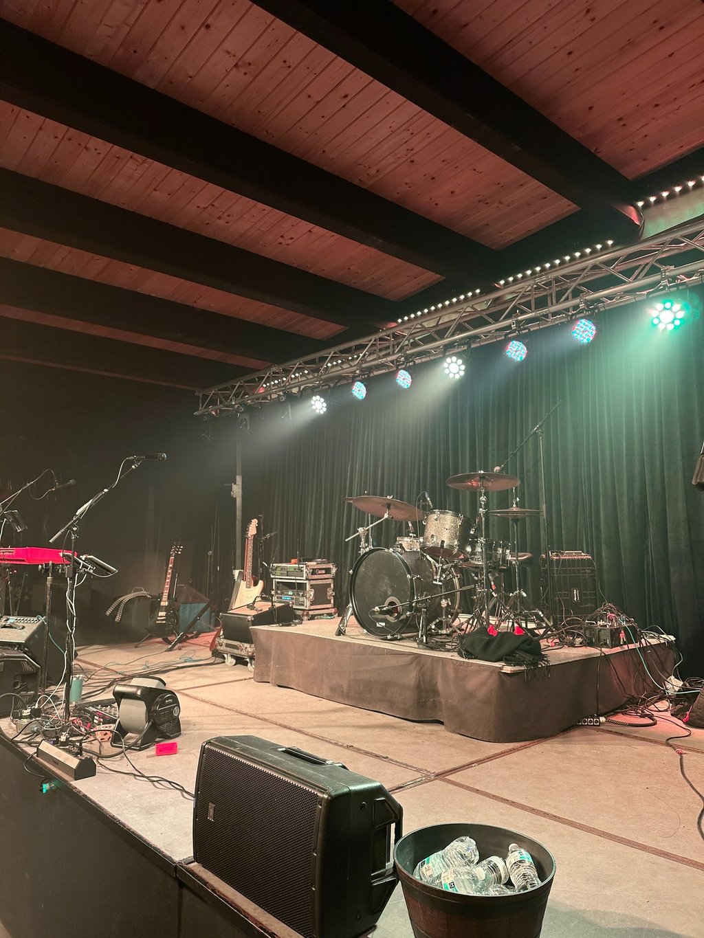 Live music stage setup with a drum kit, electric guitars, and professional concert lighting.