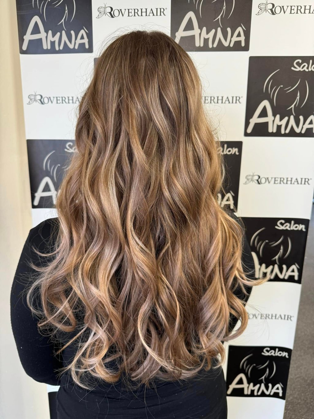 Back view of long wavy hair with honey blonde balayage highlights and professional styling.