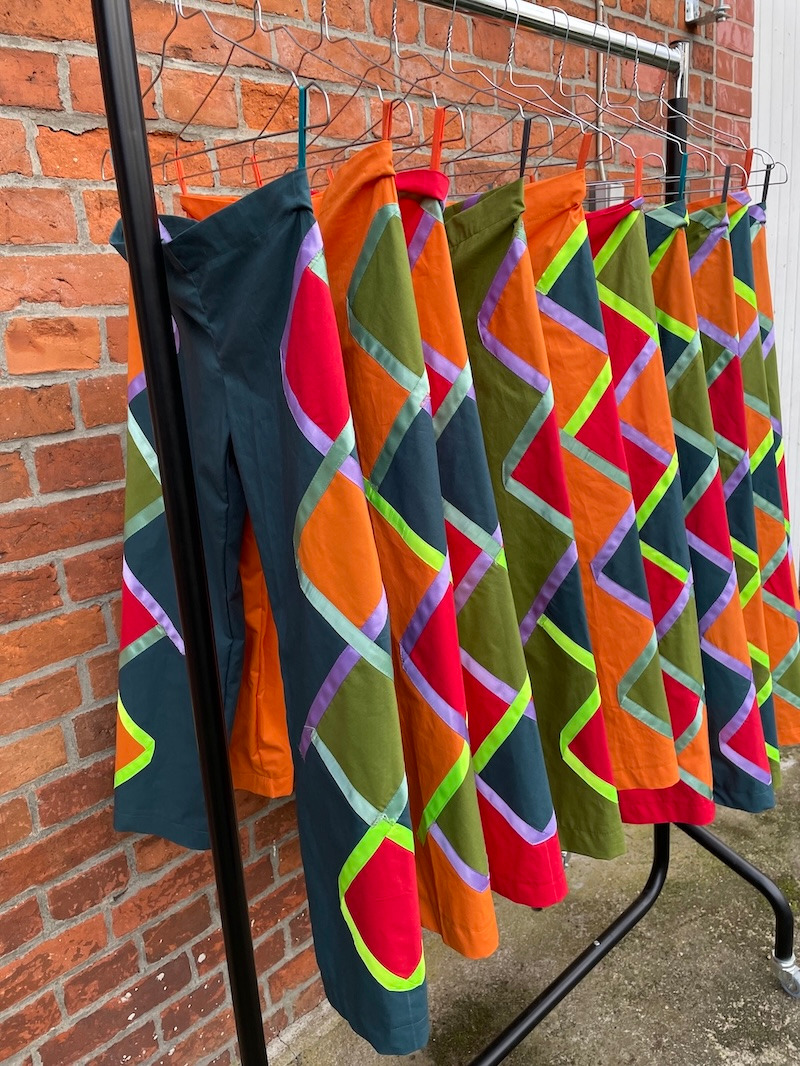 Handmade colorful patchwork trousers with geometric patterns hanging on a clothing rack.