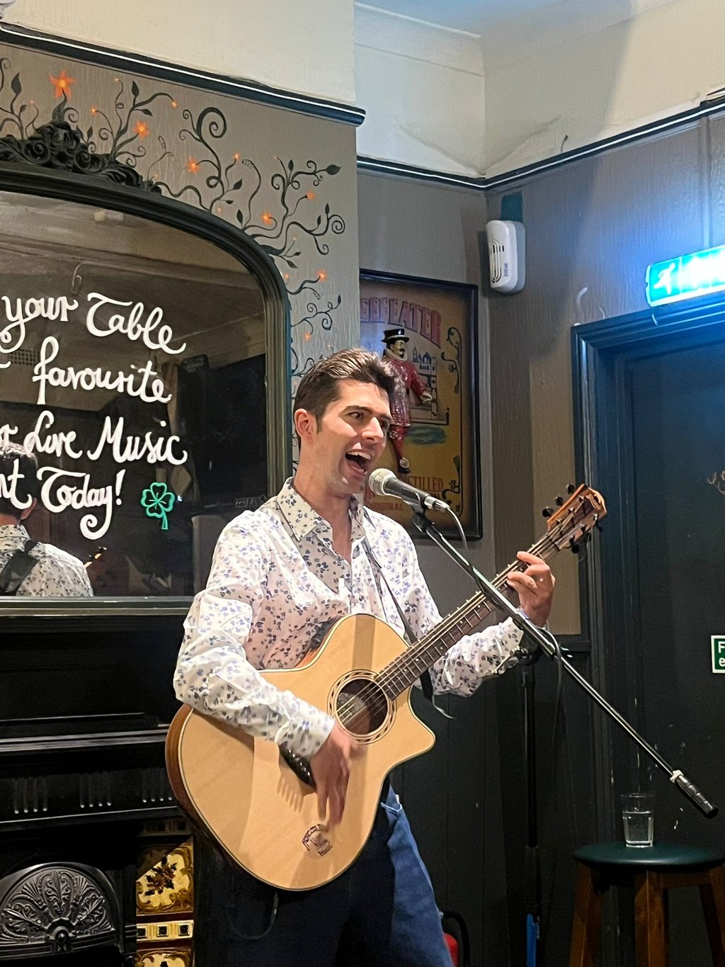 Olly Williams performing live at The Fiddler’s Elbow in Brighton, playing acoustic guitar and singing into a microphone.