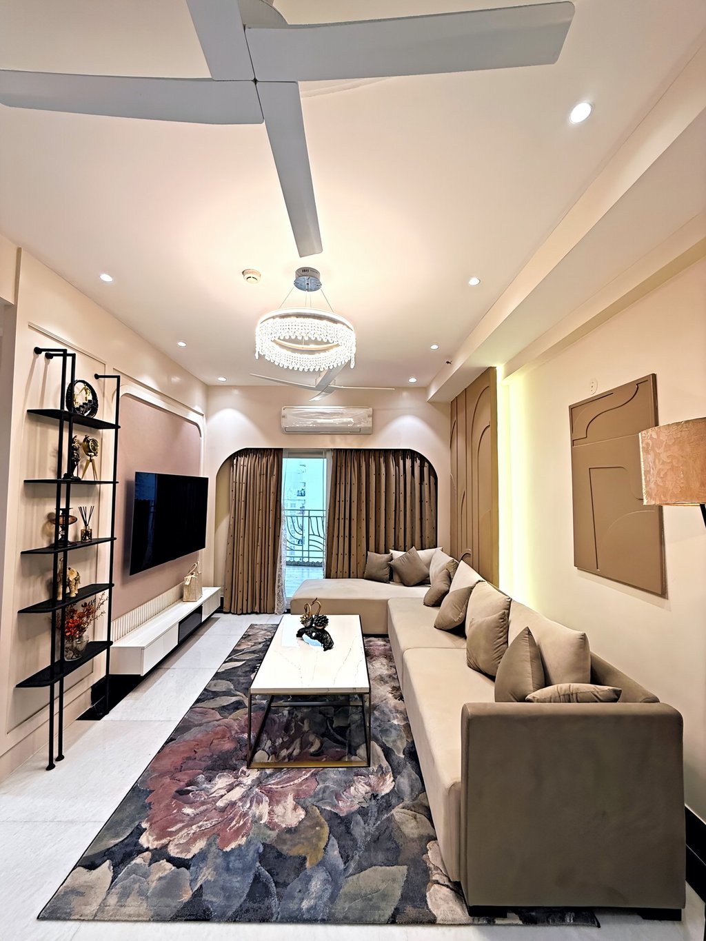 Modern living room featuring a beige sectional sofa, floral area rug, and elegant crystal chandelier.