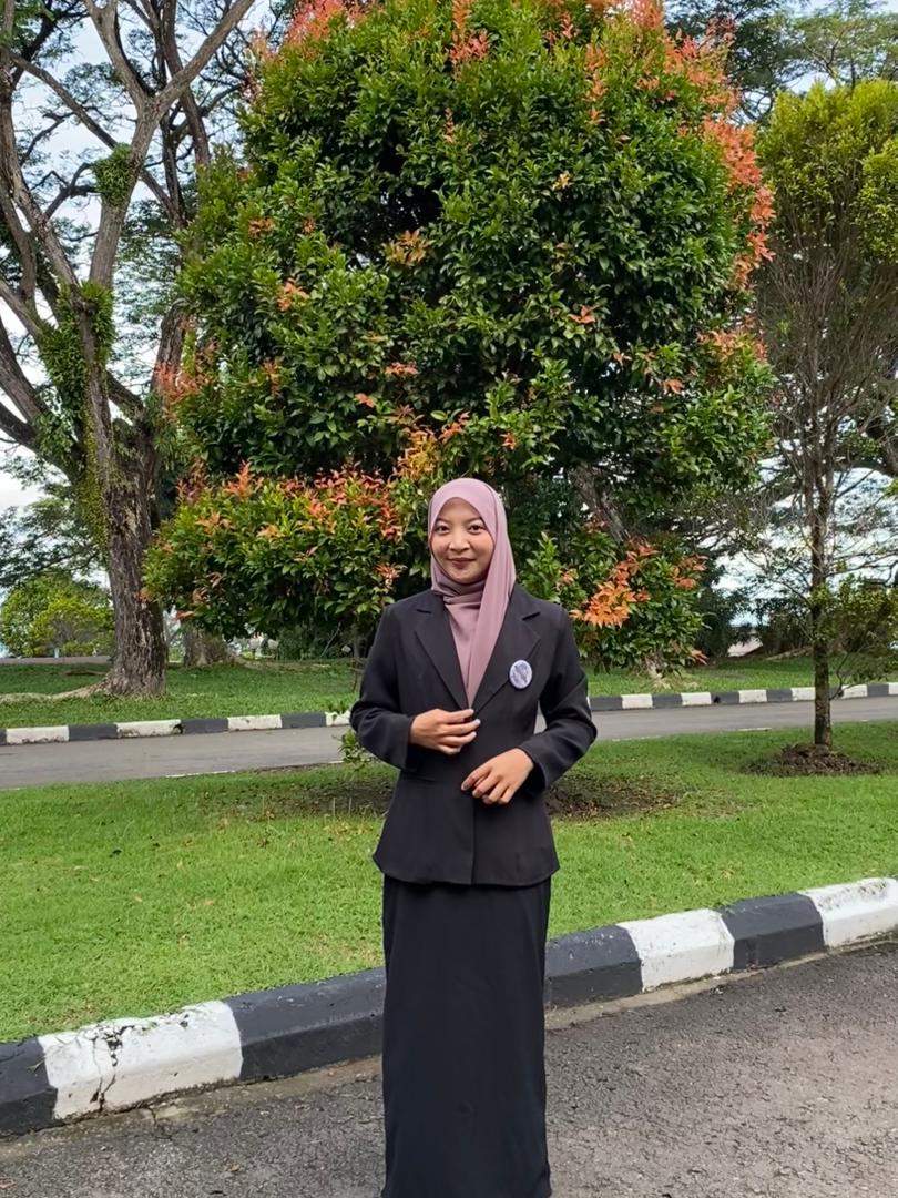 Professional woman wearing a black blazer and pink hijab standing in a green park.