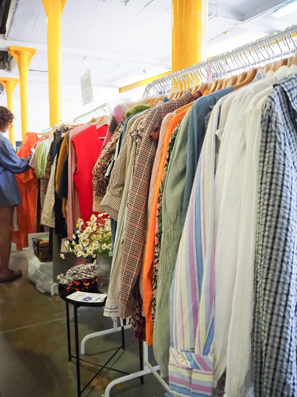 kobieta przegląda ubrania na wieszakach na targach odzieży vintage